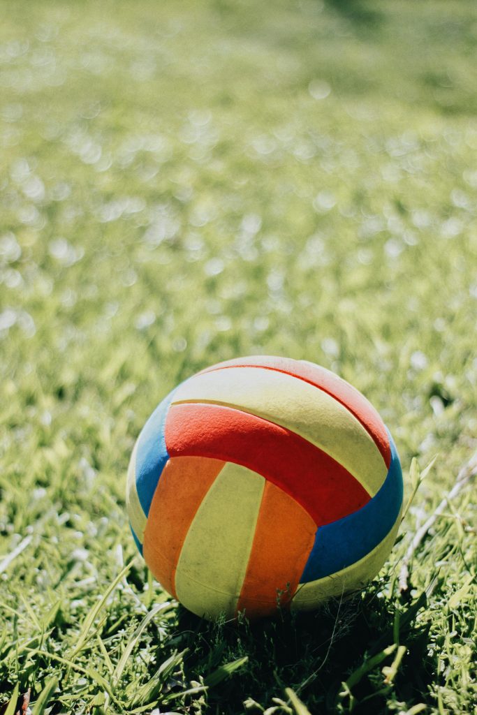 A colorful soccer ball lies on a lush green grass field, under bright sunlight.