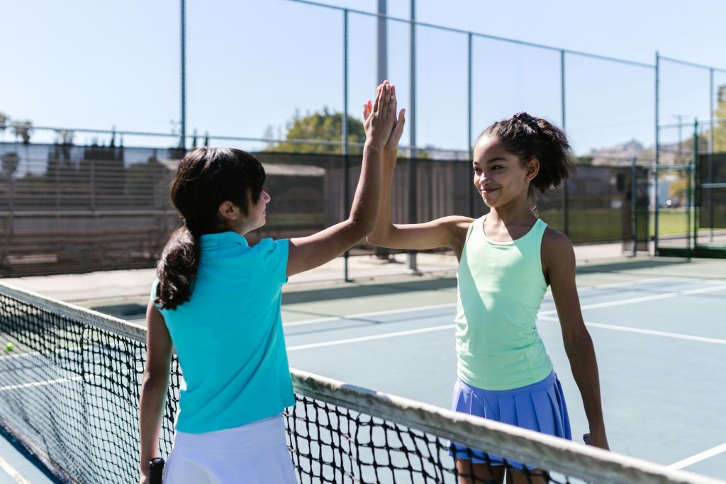 pexels-photo-8223993-8223993 Two teen girls celebrating with a high five on a sunny tennis court.
